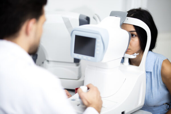 Young female patient leaning with her face on optical instrument chassis for eye exam in the clinic